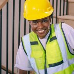 Confident construction worker wearing a hardhat and reflective vest while seated indoors.